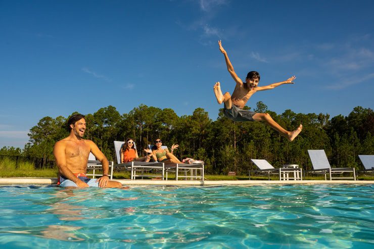 boy jumping into pool with family